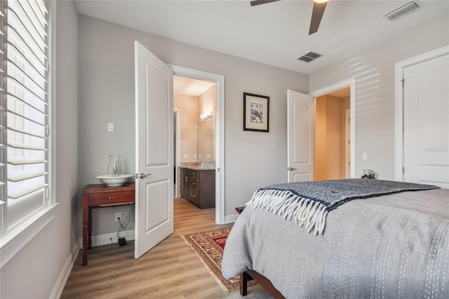 bedroom featuring ceiling fan, ensuite bathroom, multiple windows, and light wood-type flooring