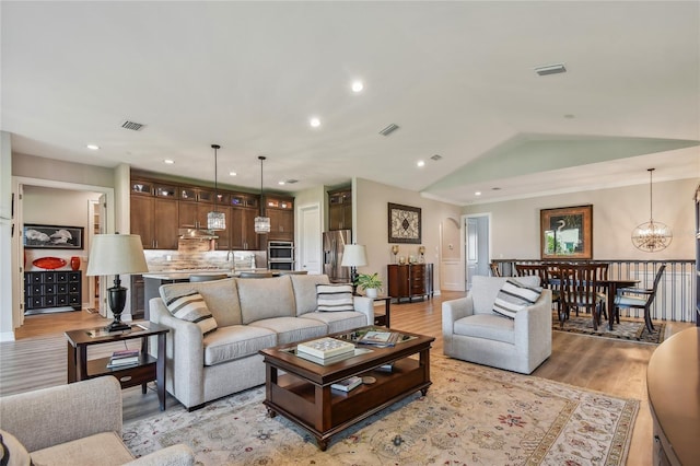 living room with vaulted ceiling, sink, a chandelier, and light wood-type flooring