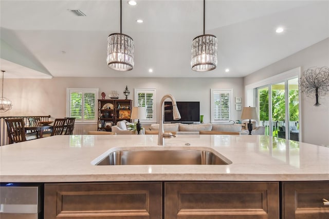 kitchen featuring sink, an inviting chandelier, dark brown cabinets, hanging light fixtures, and a kitchen island with sink