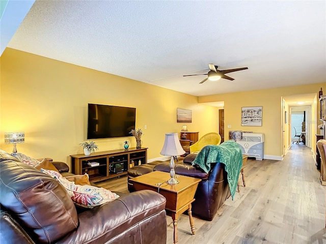 living room featuring ceiling fan, light hardwood / wood-style flooring, and a textured ceiling