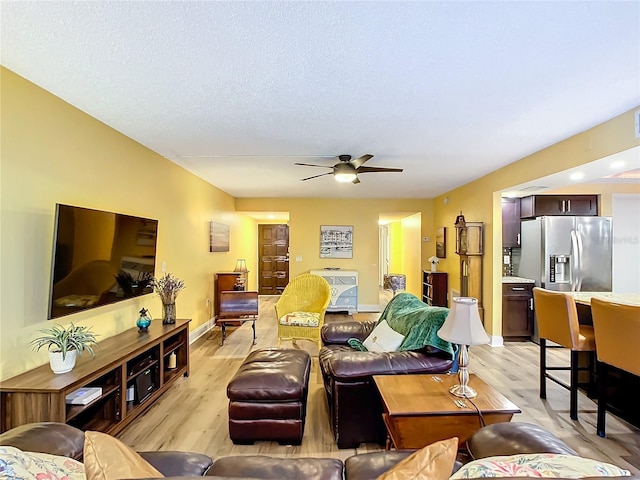 living room with ceiling fan, a textured ceiling, and light hardwood / wood-style flooring