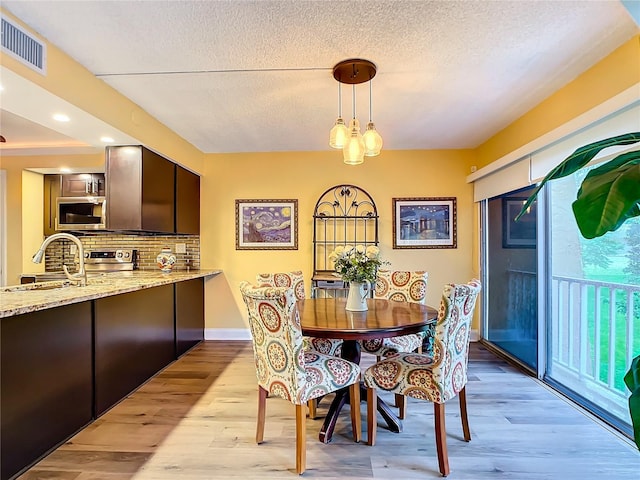 dining room featuring sink, a textured ceiling, and light hardwood / wood-style flooring