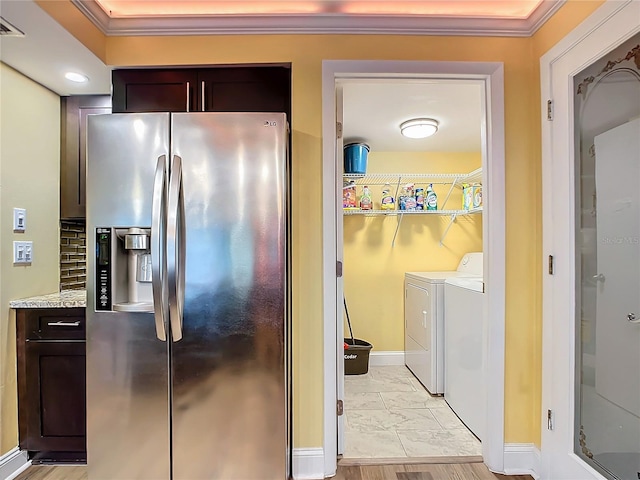 kitchen with crown molding, dark brown cabinets, stainless steel refrigerator with ice dispenser, washer and dryer, and decorative backsplash