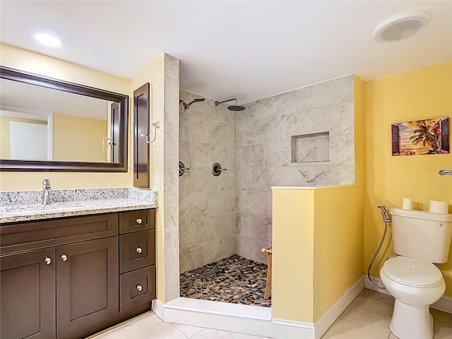 bathroom with a tile shower, vanity, tile patterned flooring, and toilet