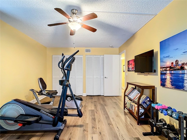 workout area featuring ceiling fan, a textured ceiling, and light wood-type flooring