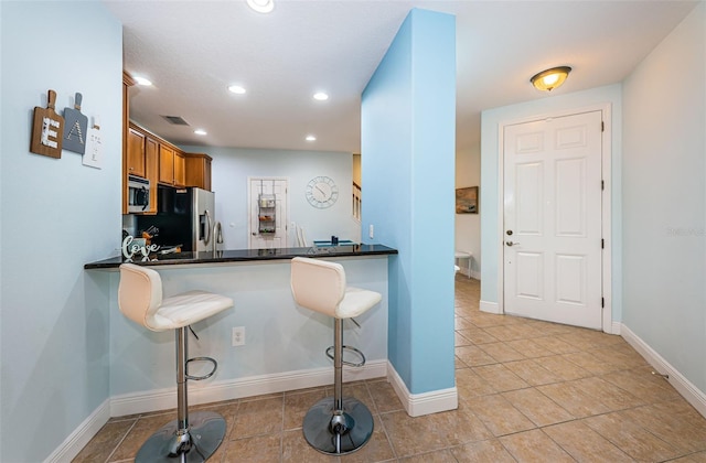 kitchen featuring kitchen peninsula, sink, appliances with stainless steel finishes, a kitchen breakfast bar, and dark stone counters