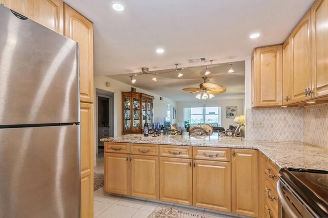 kitchen featuring ceiling fan, light stone counters, stainless steel refrigerator, light tile patterned floors, and backsplash