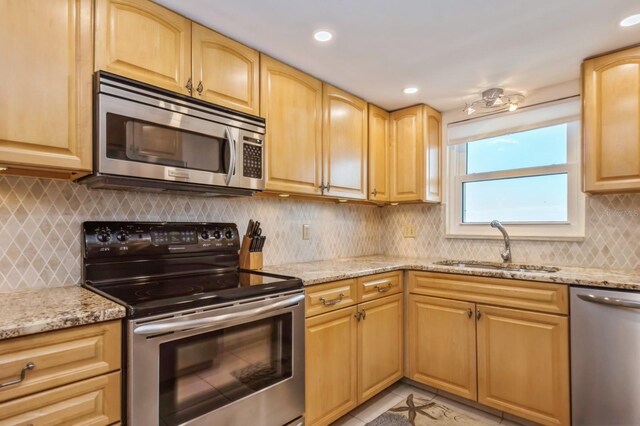 kitchen featuring backsplash, light stone countertops, appliances with stainless steel finishes, light brown cabinetry, and sink