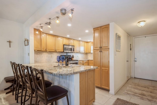 kitchen with light tile patterned floors, appliances with stainless steel finishes, a kitchen breakfast bar, light stone countertops, and kitchen peninsula