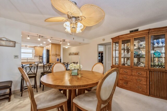 dining area featuring sink, rail lighting, light carpet, and ceiling fan