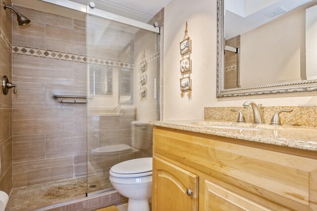 bathroom featuring a shower with shower door, vanity, and toilet