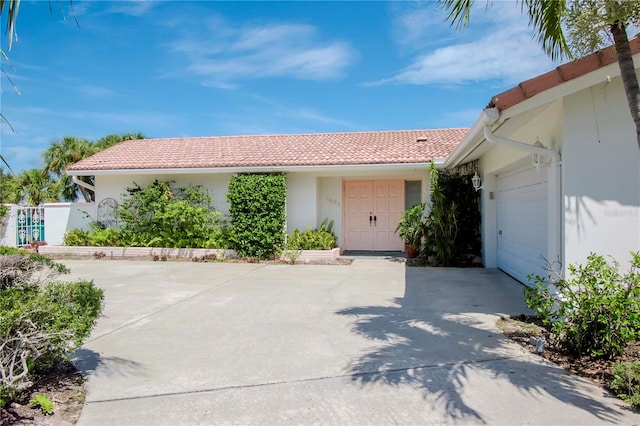 ranch-style house featuring driveway, an attached garage, a tile roof, and stucco siding