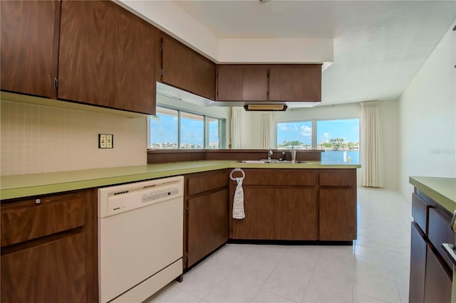 kitchen with light tile patterned flooring, kitchen peninsula, white dishwasher, decorative backsplash, and sink