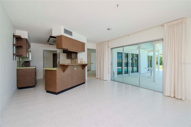 kitchen with light tile patterned floors, kitchen peninsula, ceiling fan, white refrigerator, and a kitchen bar