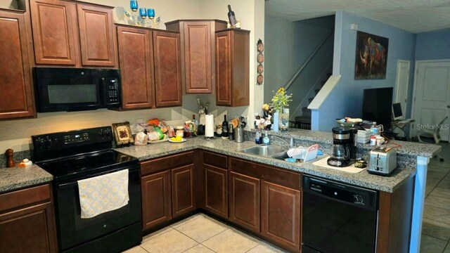 kitchen with black appliances, light tile patterned floors, sink, light stone countertops, and kitchen peninsula