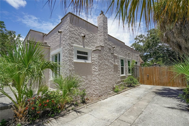 view of home's exterior featuring a wall unit AC, fence, a gate, stucco siding, and a chimney