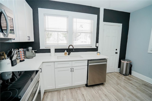 kitchen with light wood-type flooring, appliances with stainless steel finishes, white cabinetry, and sink