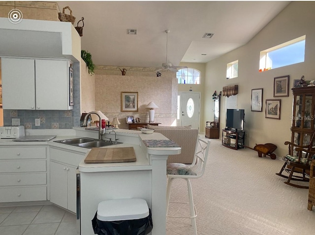 kitchen featuring white cabinetry, sink, light carpet, a breakfast bar, and kitchen peninsula