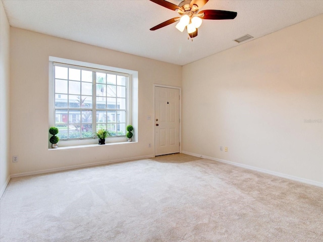 spare room featuring light carpet, ceiling fan, and a textured ceiling