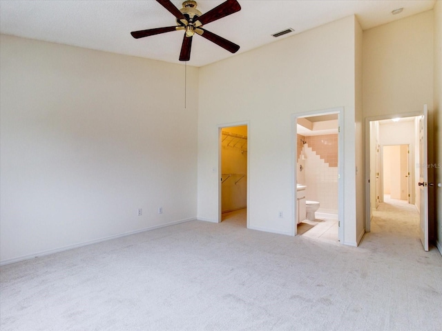 unfurnished bedroom with a high ceiling, ceiling fan, ensuite bathroom, a walk in closet, and light carpet