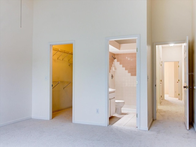 unfurnished bedroom featuring a towering ceiling, a walk in closet, light carpet, a closet, and ensuite bath