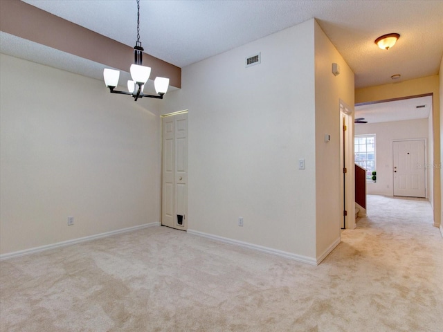 spare room featuring an inviting chandelier, a textured ceiling, and carpet flooring