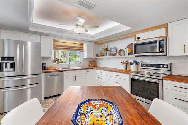 kitchen with a tray ceiling, butcher block countertops, and appliances with stainless steel finishes