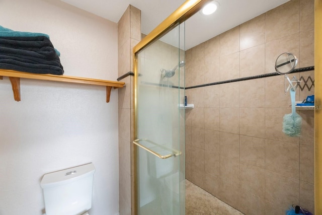 bathroom featuring a shower with door and toilet