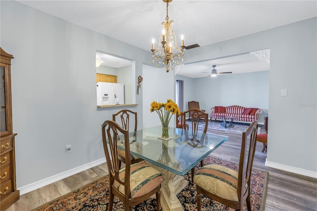 dining area with a textured ceiling, wood-type flooring, and ceiling fan with notable chandelier