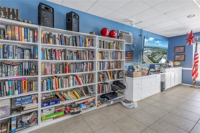 interior space with light tile patterned floors, a wall unit AC, and a drop ceiling