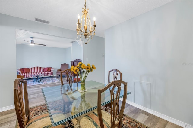 dining space with hardwood / wood-style flooring, ceiling fan with notable chandelier, and a textured ceiling