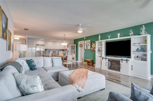 living room featuring ceiling fan, a fireplace, a textured ceiling, and hardwood / wood-style flooring