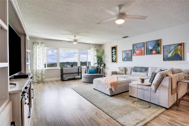 living room with light wood-type flooring, ceiling fan, and a textured ceiling