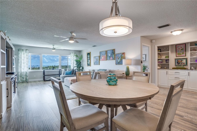 dining space with ceiling fan, built in features, a textured ceiling, and light hardwood / wood-style flooring