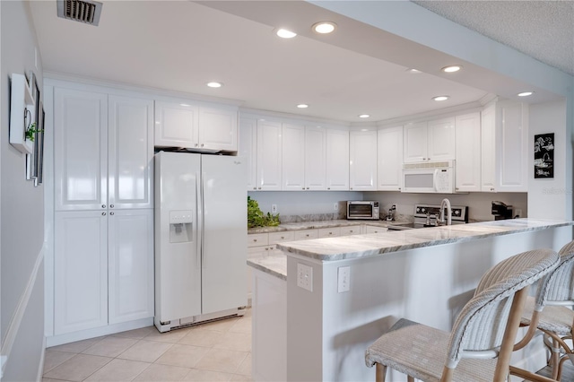 kitchen with white appliances, white cabinetry, a kitchen breakfast bar, kitchen peninsula, and light stone counters