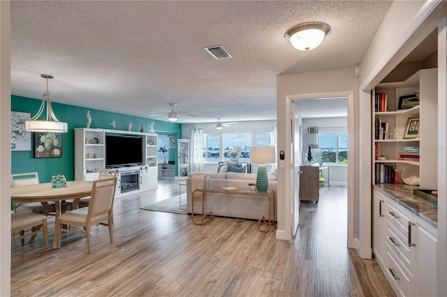 living area featuring light wood-style flooring, visible vents, ceiling fan, and a textured ceiling