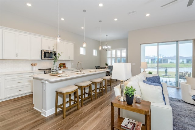 kitchen with white cabinetry, light hardwood / wood-style flooring, decorative light fixtures, and an island with sink