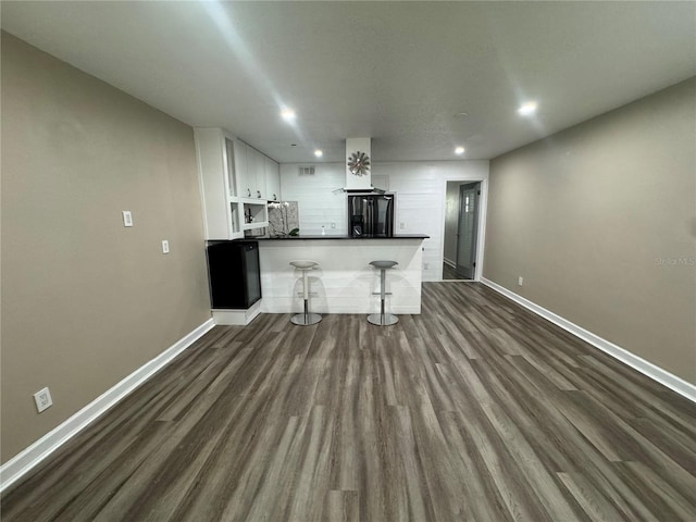 kitchen with black refrigerator, white cabinets, kitchen peninsula, a breakfast bar, and dark hardwood / wood-style floors