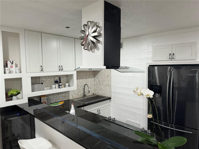 kitchen featuring a textured ceiling, range hood, stainless steel refrigerator with ice dispenser, white cabinets, and sink