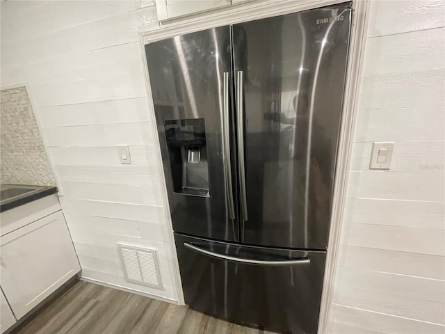 kitchen with stainless steel refrigerator with ice dispenser, hardwood / wood-style flooring, and wood walls