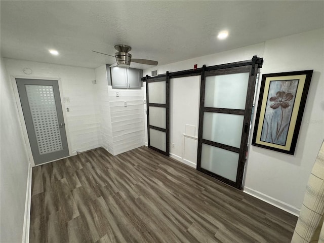 empty room featuring dark wood-type flooring, a textured ceiling, ceiling fan, and a barn door