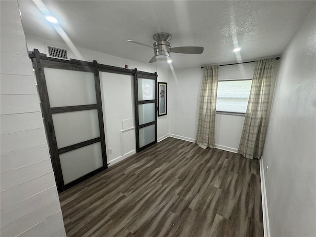 unfurnished room featuring ceiling fan, dark hardwood / wood-style flooring, a barn door, and a textured ceiling