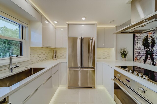 kitchen featuring stainless steel appliances, tasteful backsplash, wall chimney range hood, white cabinets, and light tile patterned flooring