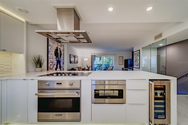 kitchen with beverage cooler, island range hood, stainless steel oven, kitchen peninsula, and gas stovetop