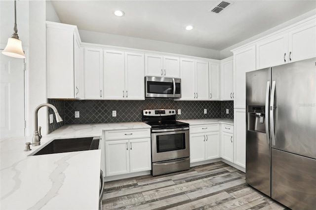 kitchen with appliances with stainless steel finishes, sink, white cabinets, hanging light fixtures, and light stone counters