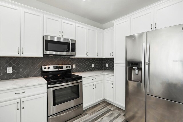 kitchen with white cabinetry, backsplash, stainless steel appliances, light stone countertops, and light wood-type flooring