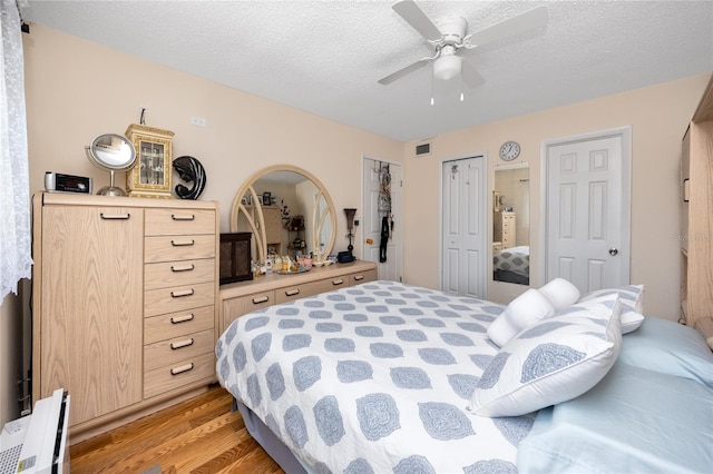 bedroom with multiple closets, ceiling fan, a textured ceiling, and light hardwood / wood-style flooring