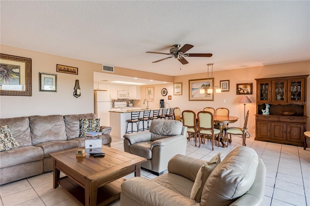 living room featuring ceiling fan, sink, light tile patterned floors, and a textured ceiling