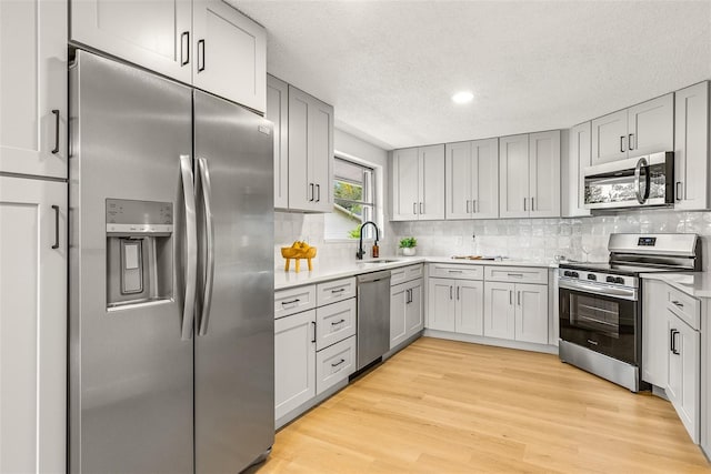 kitchen featuring light wood-type flooring, appliances with stainless steel finishes, tasteful backsplash, and sink