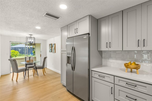 kitchen with backsplash, hanging light fixtures, gray cabinets, stainless steel fridge with ice dispenser, and a chandelier